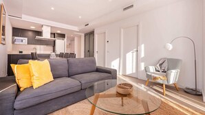 A modern living room with a grey sofa, yellow pillows, a glass coffee table, and a woven basket. - Sweett | Symphonic Central 502 (Barcelona)