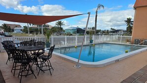 A pool area with a table and chairs, surrounded by a white fence and palm trees. - Cozy 2-bedroom condo with WiFi, AC in charming Punta Gorda (Punta Gorda)