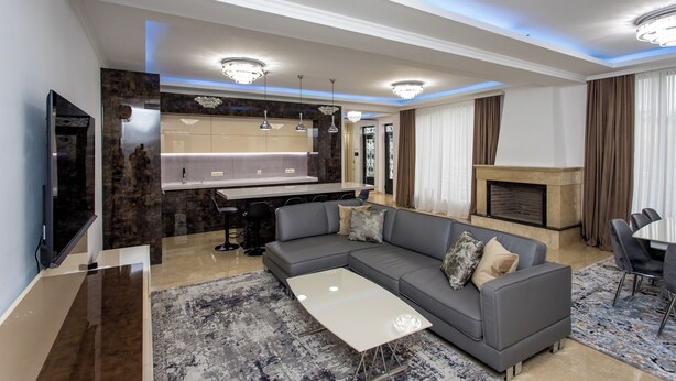 Een moderne woonkamer met een grijze modulaire bank, een flatscreen televisie, een open haard en een eethoek met een tafel en stoelen.