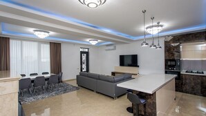 Een moderne keuken met een centraal eiland, een eethoek met tafel en stoelen, een grijze bank en een flatscreen televisie.