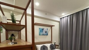 A hotel room with a wooden bed frame, a bedside table with a lamp, a wall-mounted artwork, and a large window with curtains. - Timurbay Residence Resort Style (Kuantan)