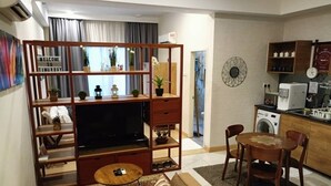A modern living room with a sofa, TV, wooden shelving, and a dining area with chairs and a table. - Timurbay Residence Resort Style (Kuantan)