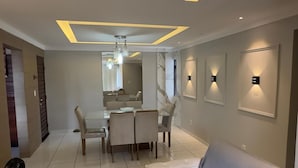 Una sala moderna con un sofá gris, una zona de comedor con mesa y sillas, e iluminación empotrada en el techo.