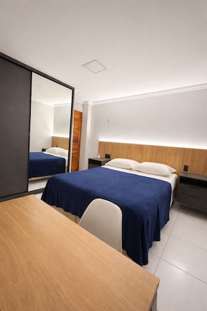 A hotel room with a bed, bedside tables, a desk, and a mirror.