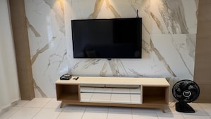 Una sala de estar moderna con un televisor de pantalla plana montado en una pared de mármol, un mueble de madera debajo y una alfombra grande de color gris en el suelo.