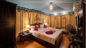 Ein Hotelzimmer mit einem großen Bett, zwei Nachttischen, einem Schreibtisch, einem Stuhl, einem Standventilator und einem Deckenventilator.