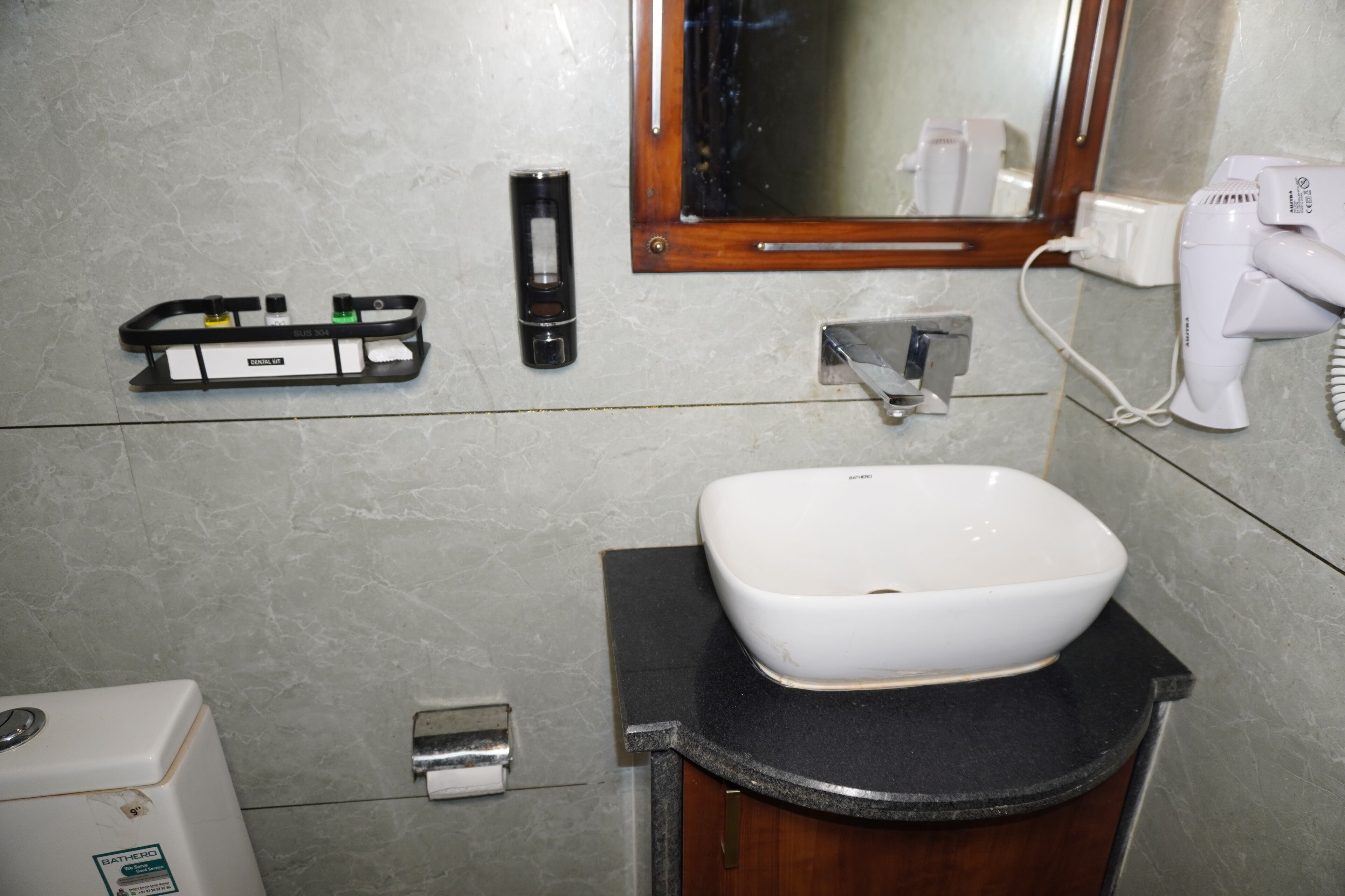 A bathroom with a white sink, a hairdryer, a soap dispenser, and a towel dispenser.