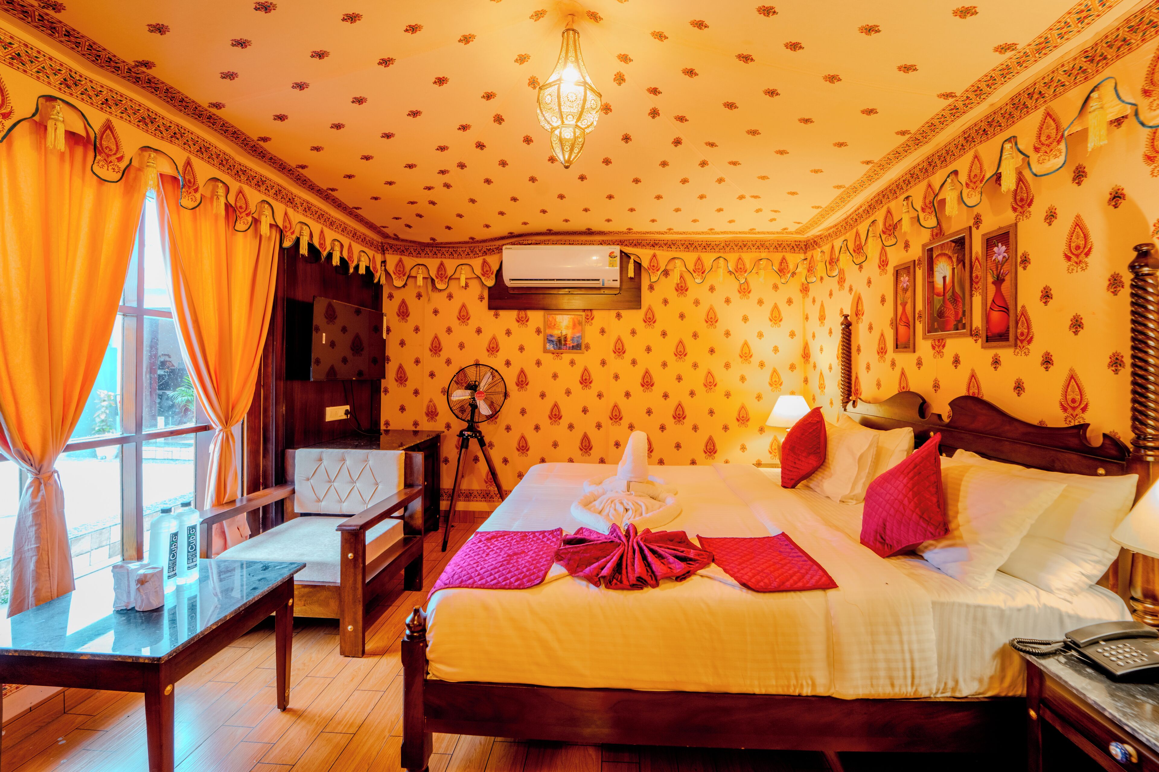 Habitación de hotel con una cama grande, un escritorio, una silla, una ventana con cortinas, un equipo de aire acondicionado y un ventilador de pared.