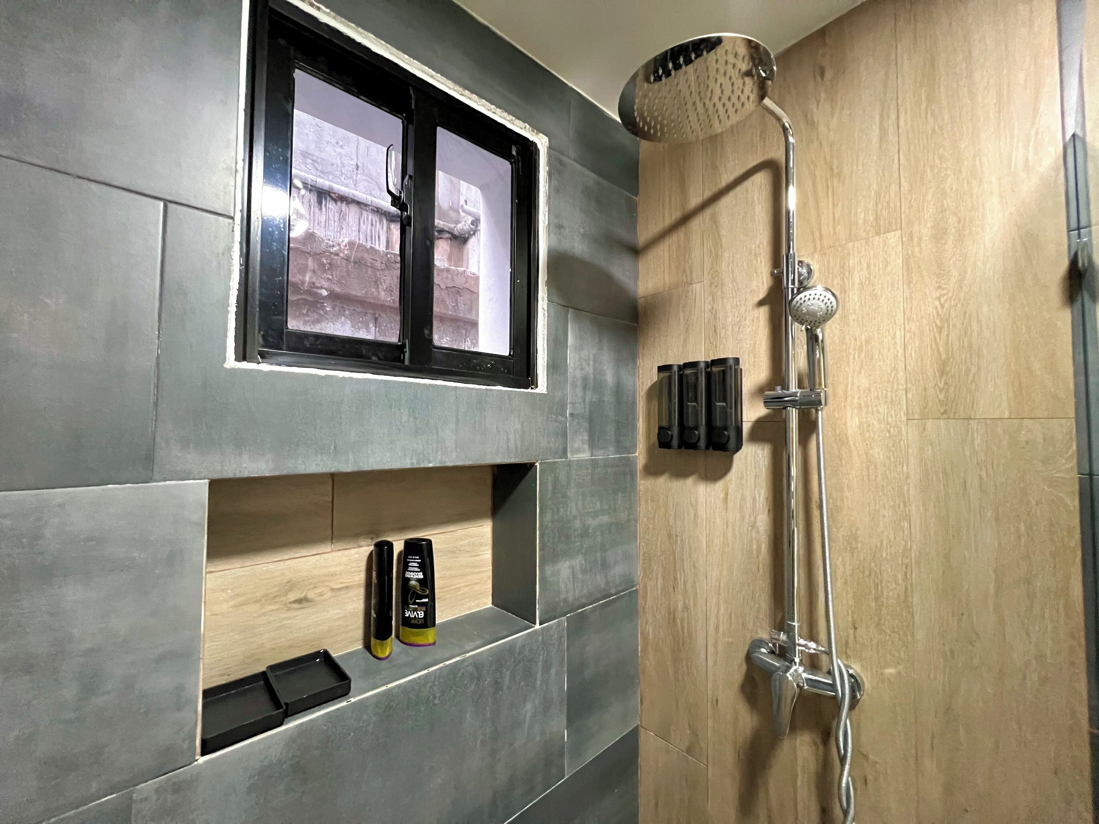 A bathroom with a shower, a window, and a shelf with toiletries.