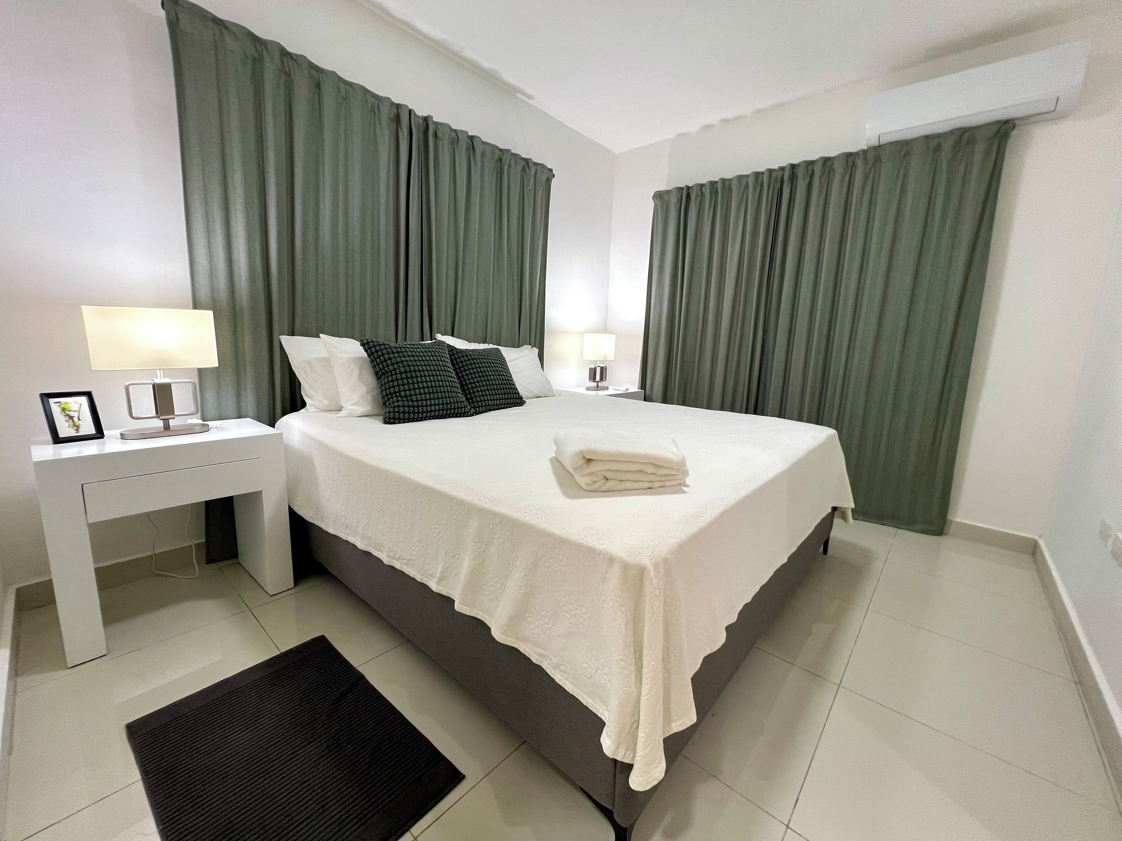 Ein Hotelzimmer mit einem Bett, zwei Nachttischen mit Lampen, einem Schreibtisch und einem schwarzen Teppich.