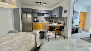 Eine moderne Küche mit integriertem Kühlschrank, Mikrowelle und Herd. Es gibt einen Essbereich mit einem Marmortisch und Stühlen.
