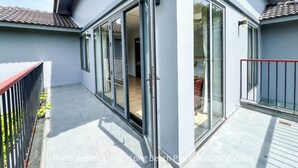 Eine moderne Villa mit großen Schiebeglastüren, einem Balkon mit Metallgeländer und einem Ziegeldach.