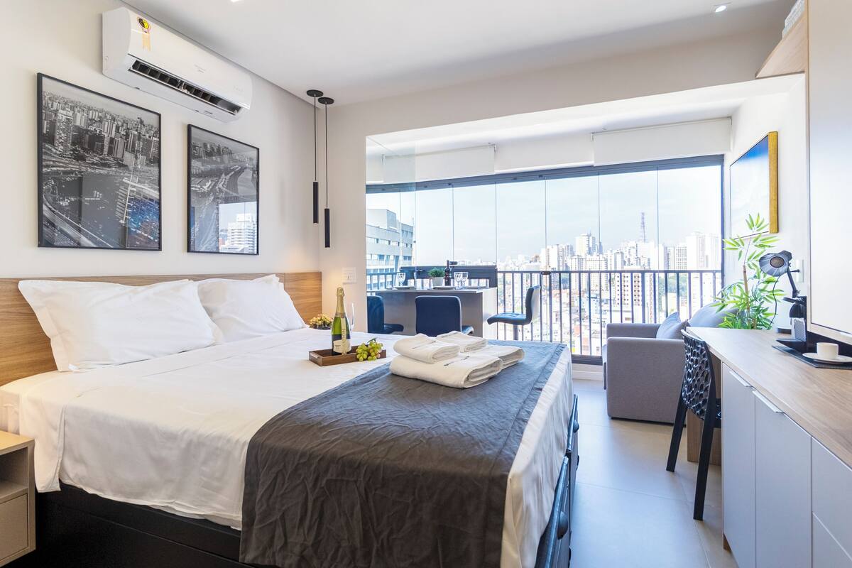 Una habitación de hotel moderna con una cama grande, un escritorio y un balcón con vistas a la ciudad.