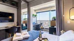 Habitación de hotel moderna con cama, escritorio, silla, televisor y balcón con vistas.