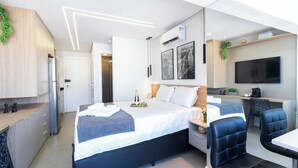 Una habitación de hotel moderna con cama, escritorio, televisor y kitchenette.