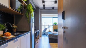 Una cocina moderna con microondas integrado, un fregadero y una encimera con una hogaza de pan. Hay una zona de comedor con una silla y una mesa pequeña.
