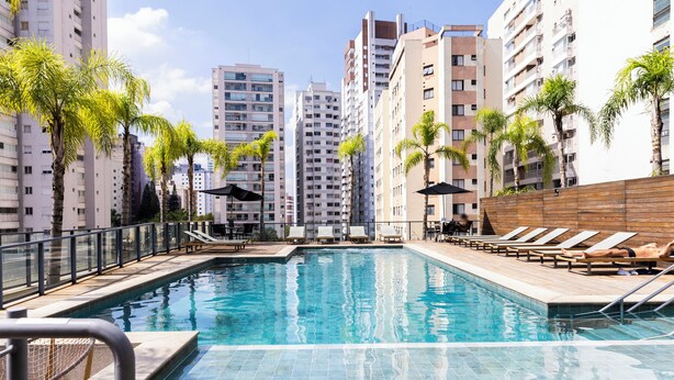 Piscina con sillas de descanso y palmeras, rodeada de edificios residenciales altos.