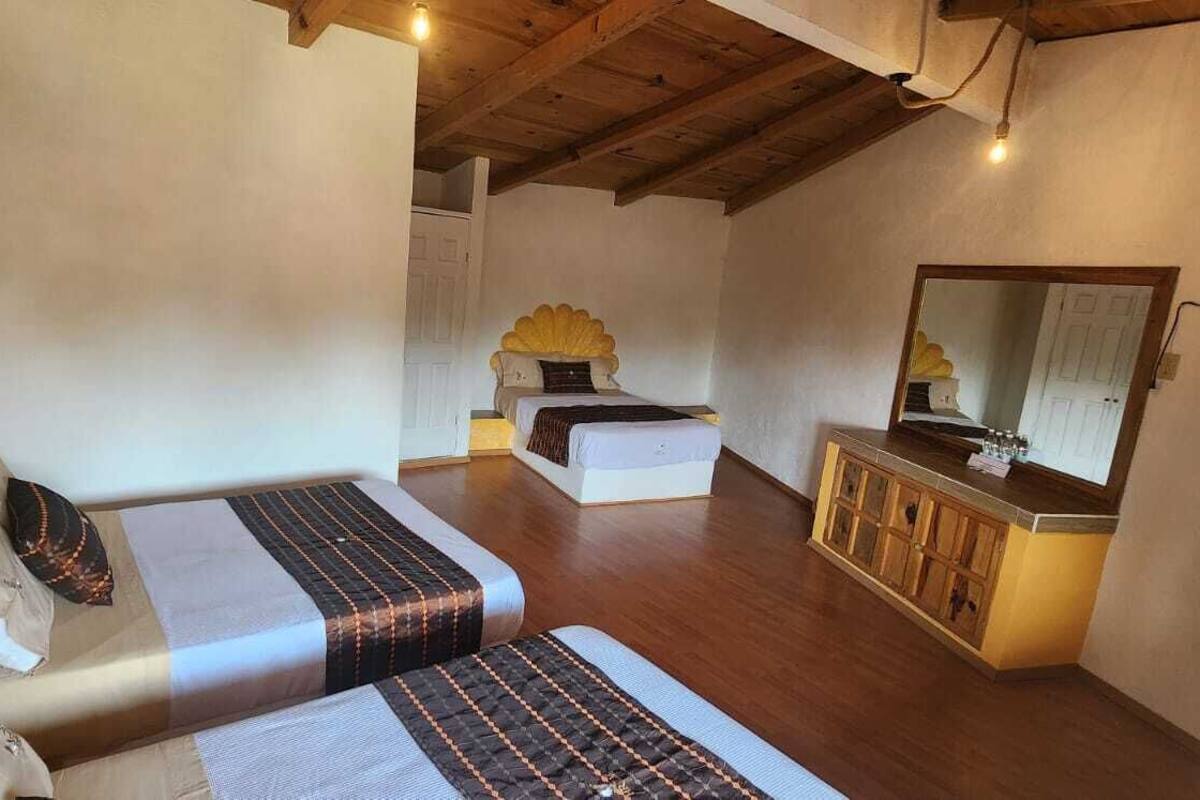 Une chambre avec deux lits, un plafond en bois, une petite table avec un miroir et un placard.