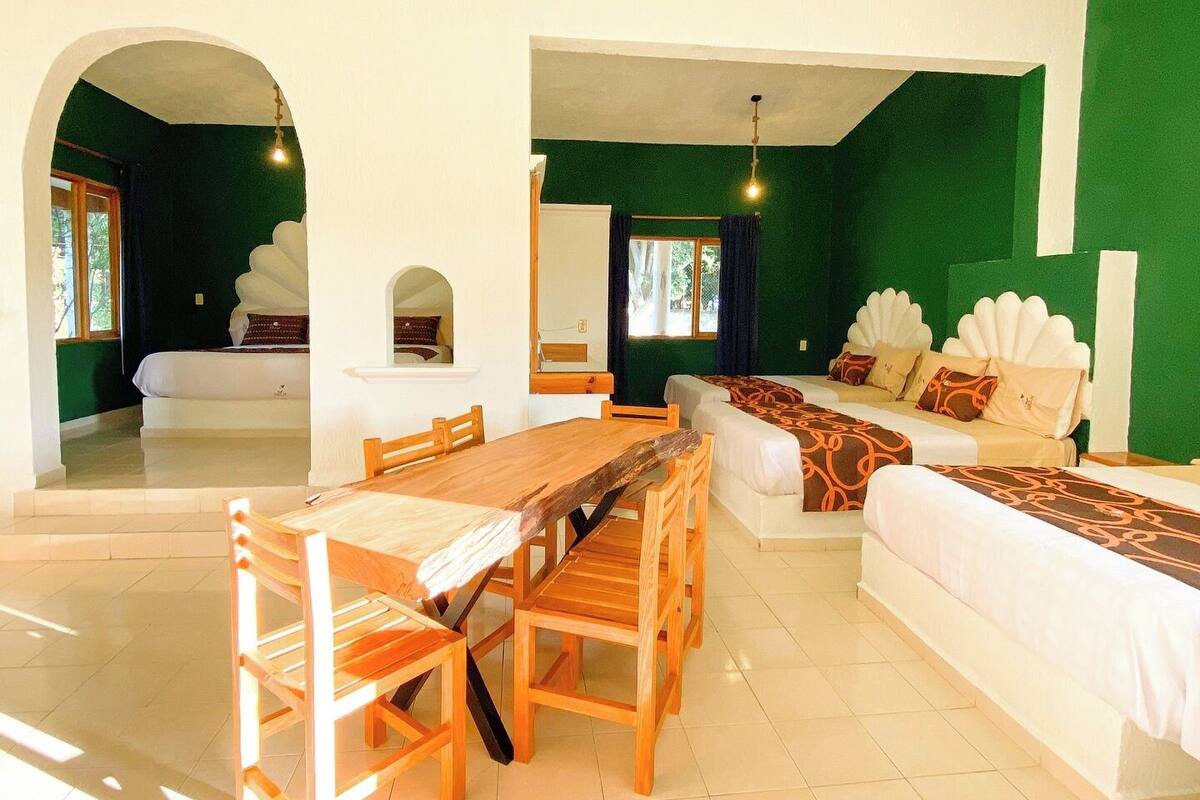 Une chambre d’hôtel comprenant un coin repas, un lit agrémenté d’une tête de lit décorative et une fenêtre avec des rideaux.