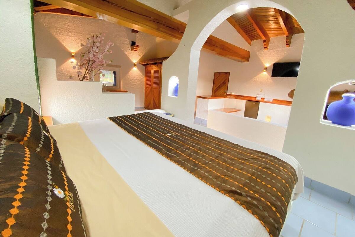 Une chambre avec un lit, un plafond en bois, une petite fenêtre et un téléviseur.
