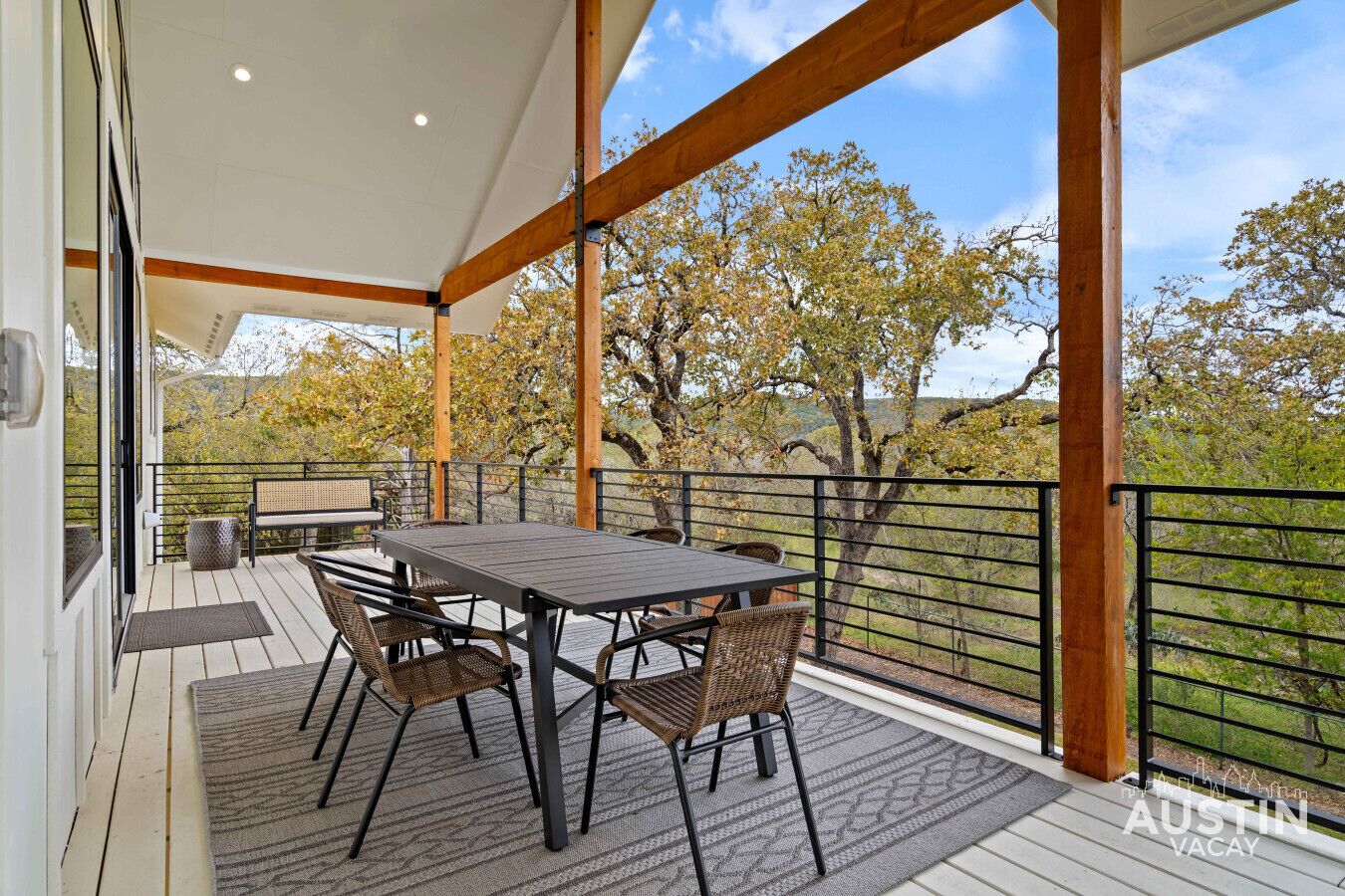 A covered outdoor patio with a table and chairs, a bench, and a view of trees and hills.