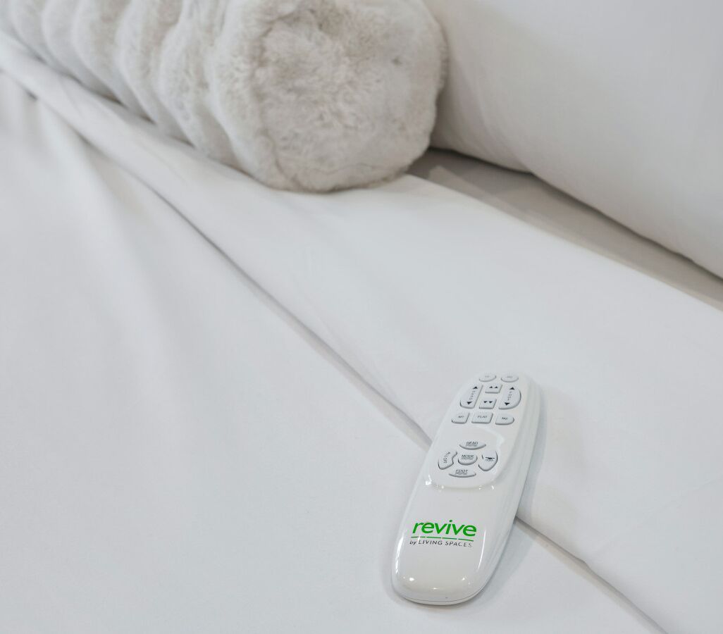 A white remote control on a bed with white bedding.