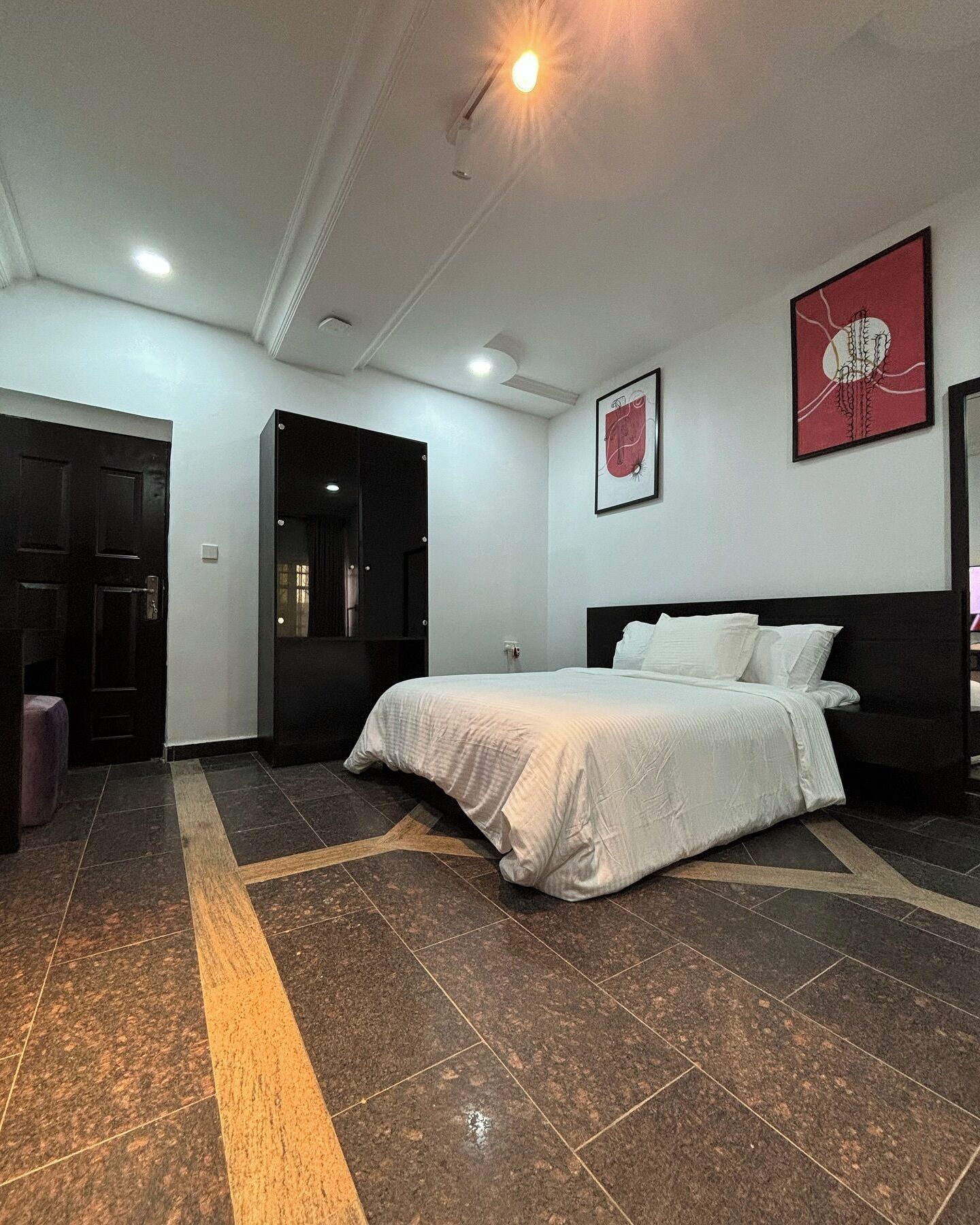 A hotel room with a bed, a door, and a wall with two framed pictures.