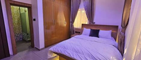 A bedroom with a large bed, wooden wardrobe, and a shower area.