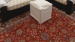 A living room with a sofa set, a small table with a floral tablecloth, a television mounted on the wall, and a patterned carpet. - Ρετιρέ μεγάλο 3 δωμάτια.καθιστικό με βεράντα αγ. Κωσταντίνος με θέα το Πήλιο (Volos)
