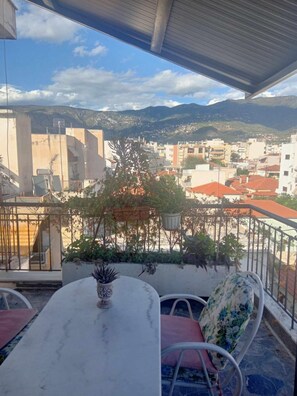 Une terrasse avec une table et des chaises, des plantes en pot et une vue sur un paysage urbain avec des montagnes en arrière-plan.