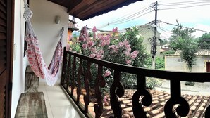 A balcony with a wrought iron railing, a macramé hanging, and pink flowering trees in the background. - LARGE PRIVATE SUITE WITH BALCONY AND CLOSE TO THE HISTORIC CENTER. PET FRIENDLY  (Caborê Paraty)