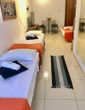 Een hotelkamer met drie bedden, een tafeltje met een schaal, een stoel en een spiegel aan de muur.