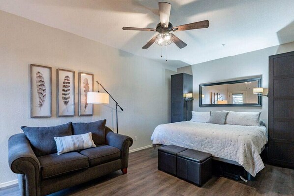A bedroom with a bed, a sofa, a ceiling fan, and framed artwork on the wall.