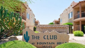 Segnaletica per 'The Club at Fountain Hill 16545' con motivo di cactus, circondata da edifici con balconi e cielo sereno.