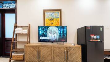 Un mueble de madera con un televisor de pantalla plana mostrando 'Vinland Saga' en Netflix, un refrigerador y una obra de arte enmarcada sobre el televisor.