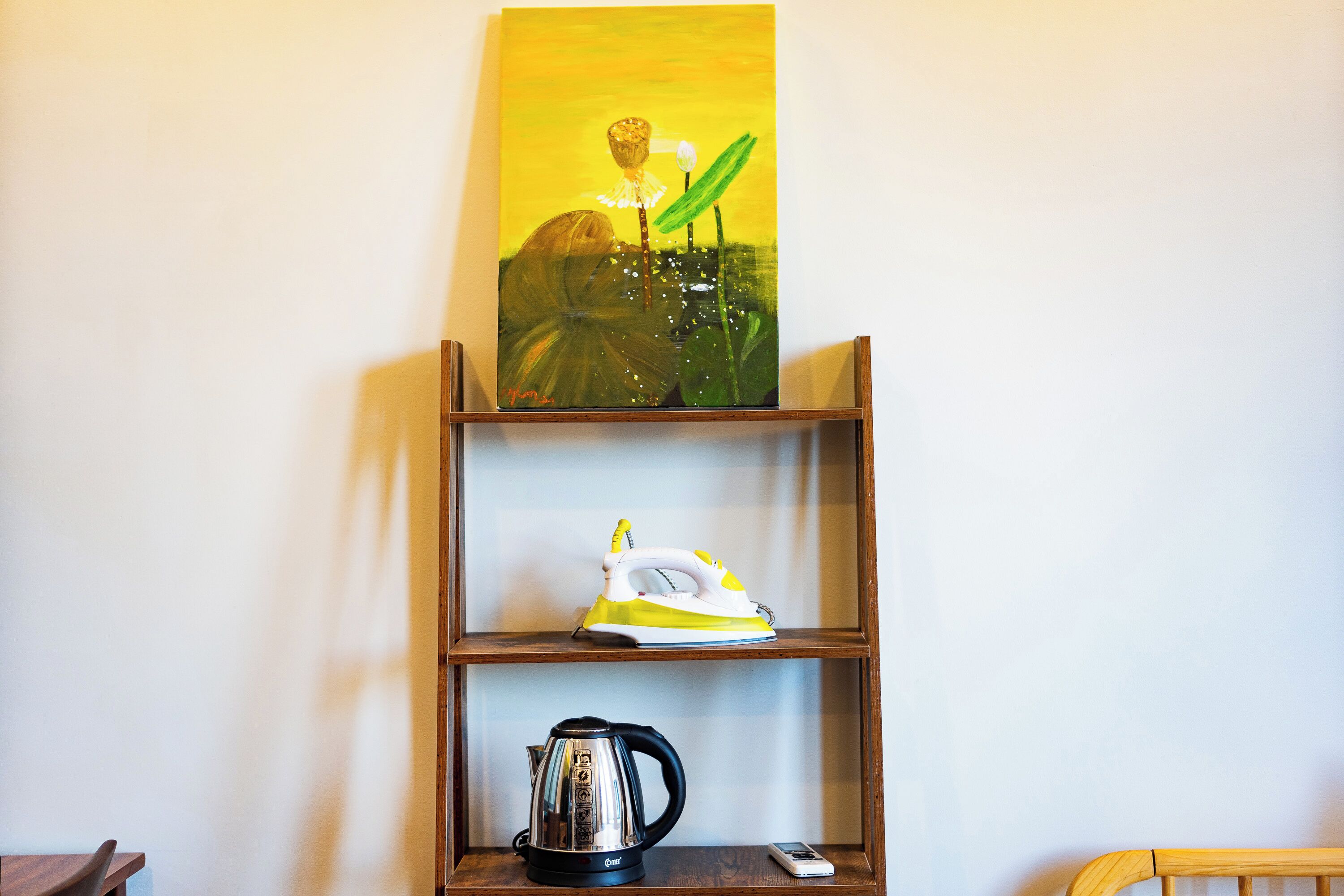 A shelf with a painting, an iron, and a kettle.