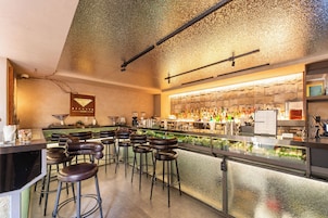 Una zona de bar con taburetes, mostrador y una variedad de botellas y vasos.