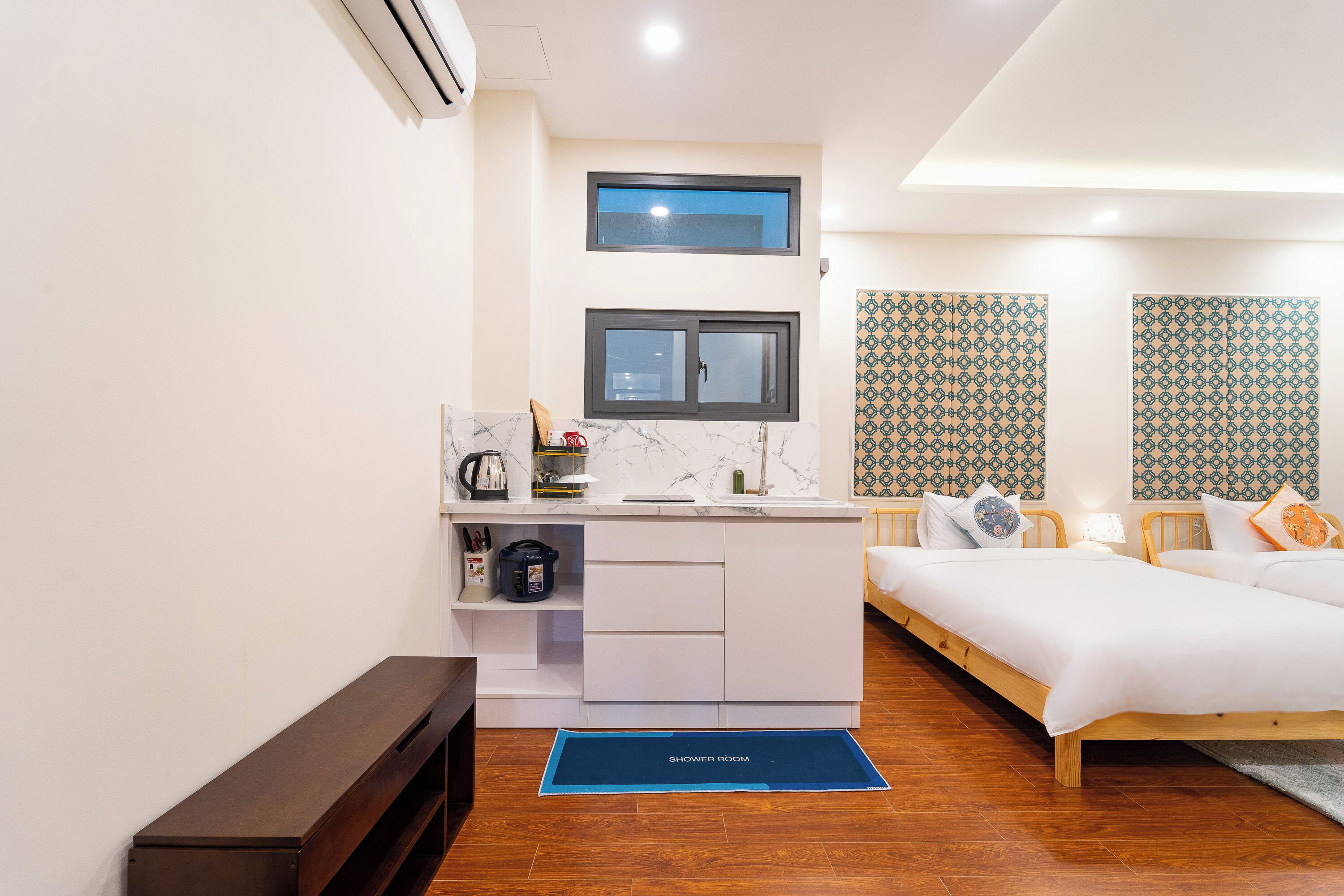 A compact hotel room with a kitchenette, a bed with pillows, a shower area, and patterned wallpaper.