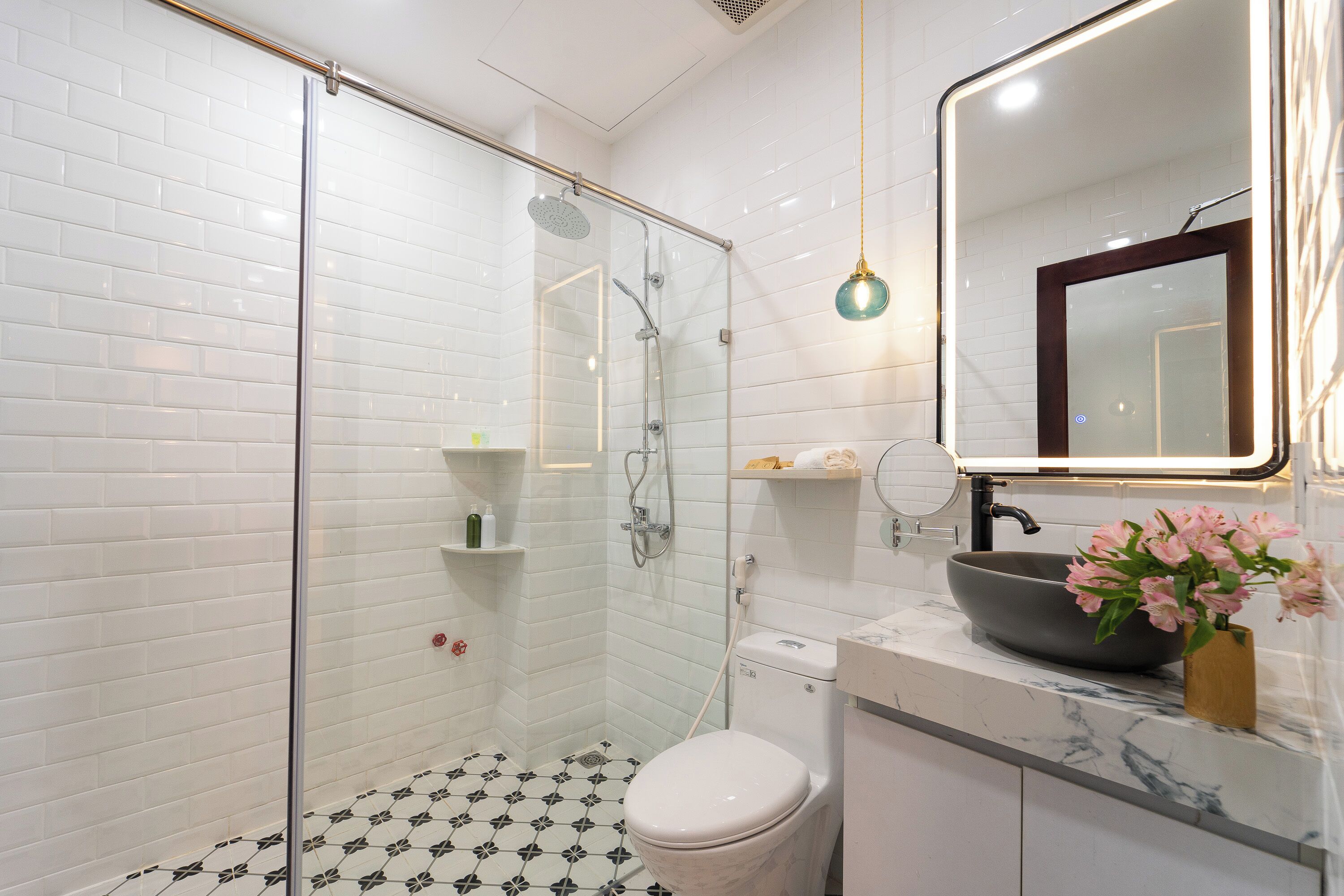 Un baño moderno con azulejos blancos tipo metro, una ducha con cerramiento de vidrio, inodoro blanco, encimera de mármol y lavamanos con lavabo de pedestal.