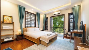 Ein helles Schlafzimmer mit einem großen Bett, einem Schreibtisch mit Computer und Blick auf Grünflächen.
