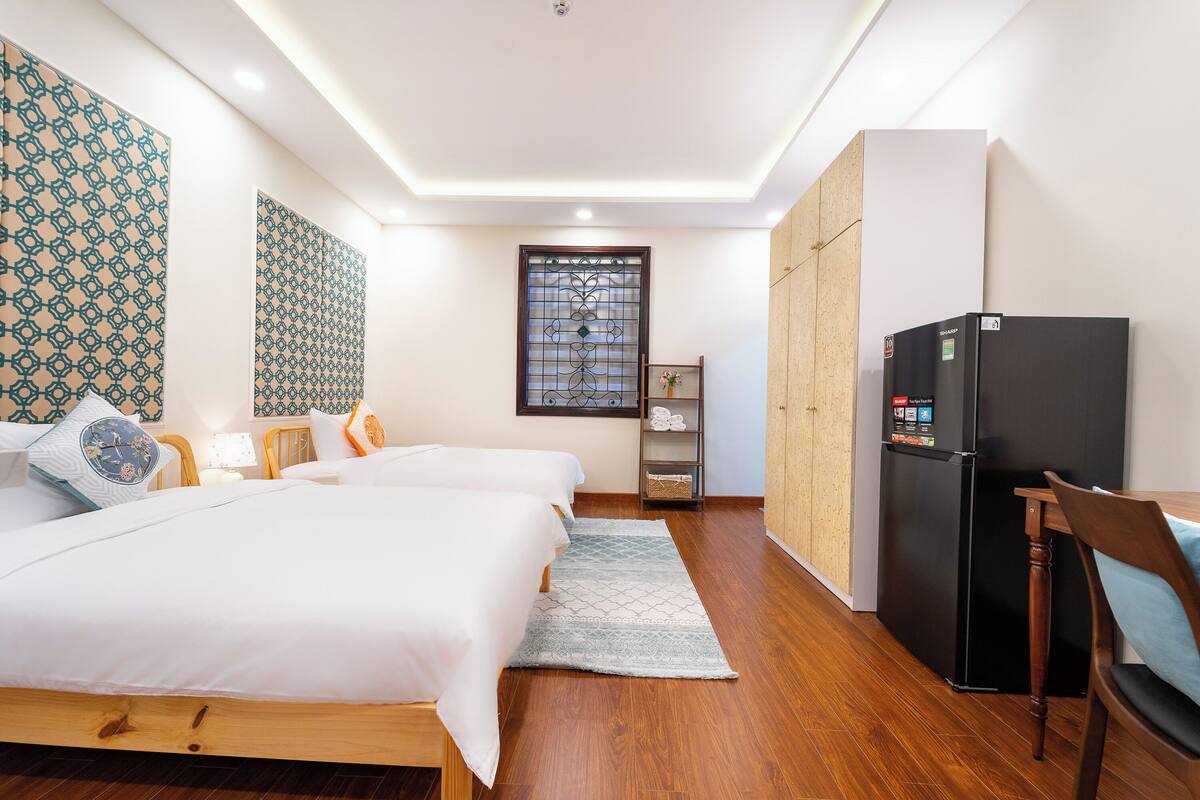 A hotel room with a bed, a desk, a refrigerator, and a window with a decorative screen.