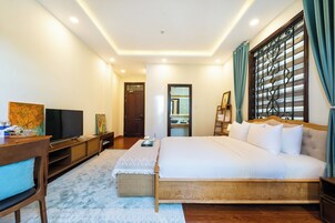Una habitación de hotel con una cama grande, televisión, escritorio de madera y ventana con cortinas.