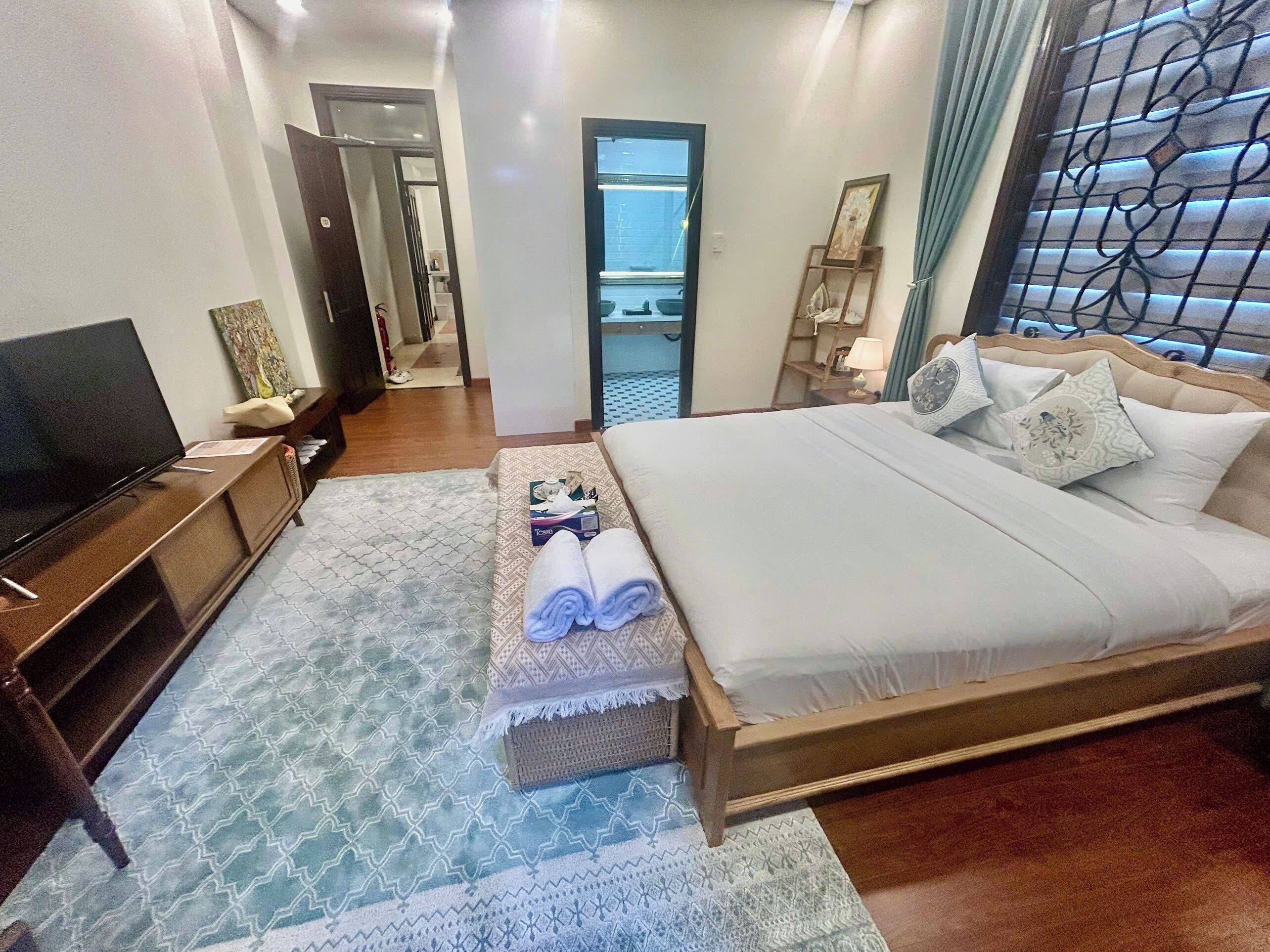 A hotel room with a bed, a TV, a desk, and a bathroom visible through an open door.