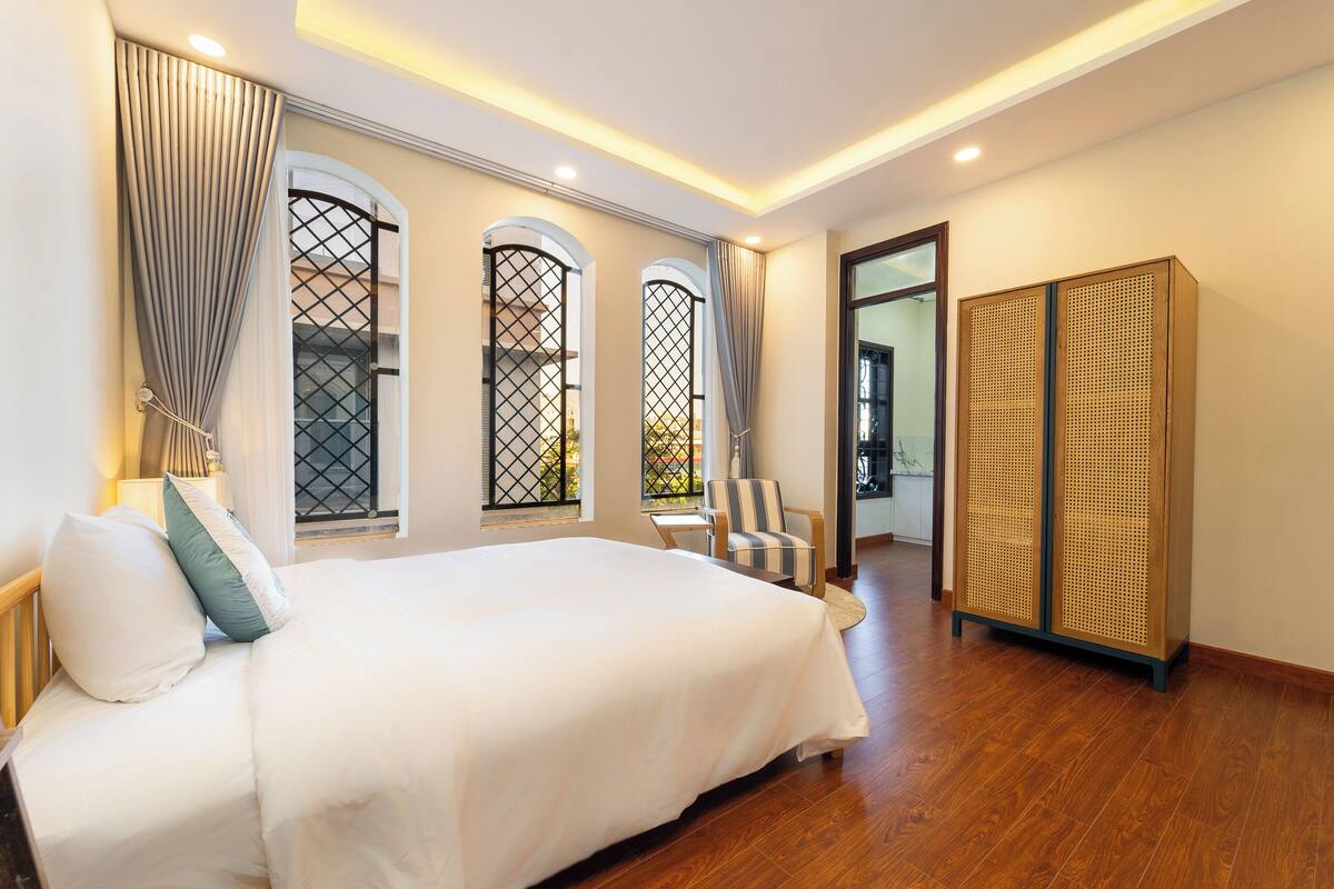 A spacious bedroom with a large bed, a chair, and a wardrobe.