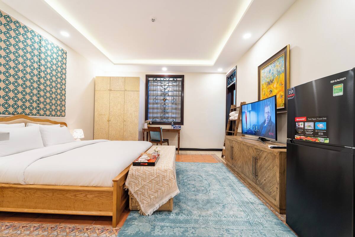 A bedroom with a bed, a desk, a television, and a refrigerator.
