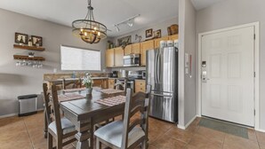 A modern kitchen with a dining table, chairs, a chandelier, a refrigerator, and a microwave. - Walk to Fountain Park! Ground-Floor Condo w/ Pool, Spa & Private Patio (Fountain Hills)