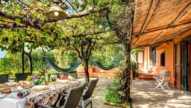 Un espacio al aire libre para comer con una mesa lista para una comida, rodeado de sillas de mimbre y una hamaca.