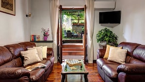 Sala de estar con dos sofás de cuero, una mesa de centro con piezas de ajedrez, un televisor y una escalera que lleva a un espacio exterior con plantas.