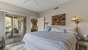 A bedroom with a large bed, a ceiling fan, a wooden wall decoration, and a sliding glass door leading to a balcony. - Ground Floor Condo Near Plaza & Fountain Park w/ Pool, Hot Tub & Private Patio (Fountain Hills)