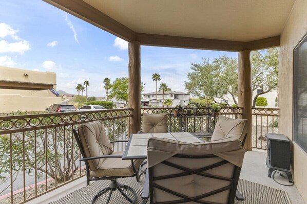 A covered outdoor patio with a table and chairs, a metal railing, and a view of the neighborhood. - Ground Floor Condo Near Plaza & Fountain Park w/ Pool, Hot Tub & Private Patio (Fountain Hills)
